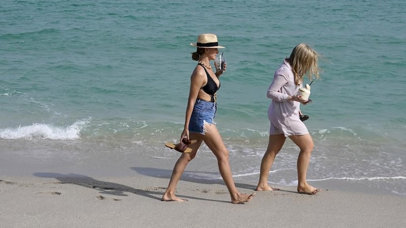 People walk along the beach, Monday, Nov. 15, 2021, in Miami Beach, Fla. Cooped-up tourists...